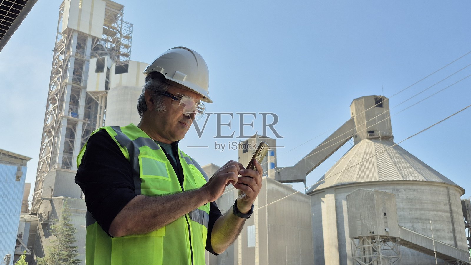 一位严肃的行业工人在高处的金属建筑上接收重要信息。照片摄影图片