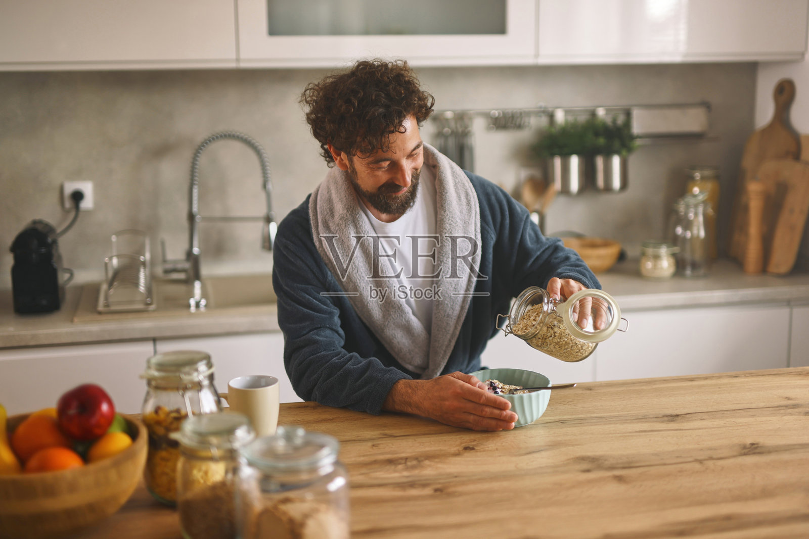 微笑的男人在厨房里将谷物倒入早餐碗中照片摄影图片