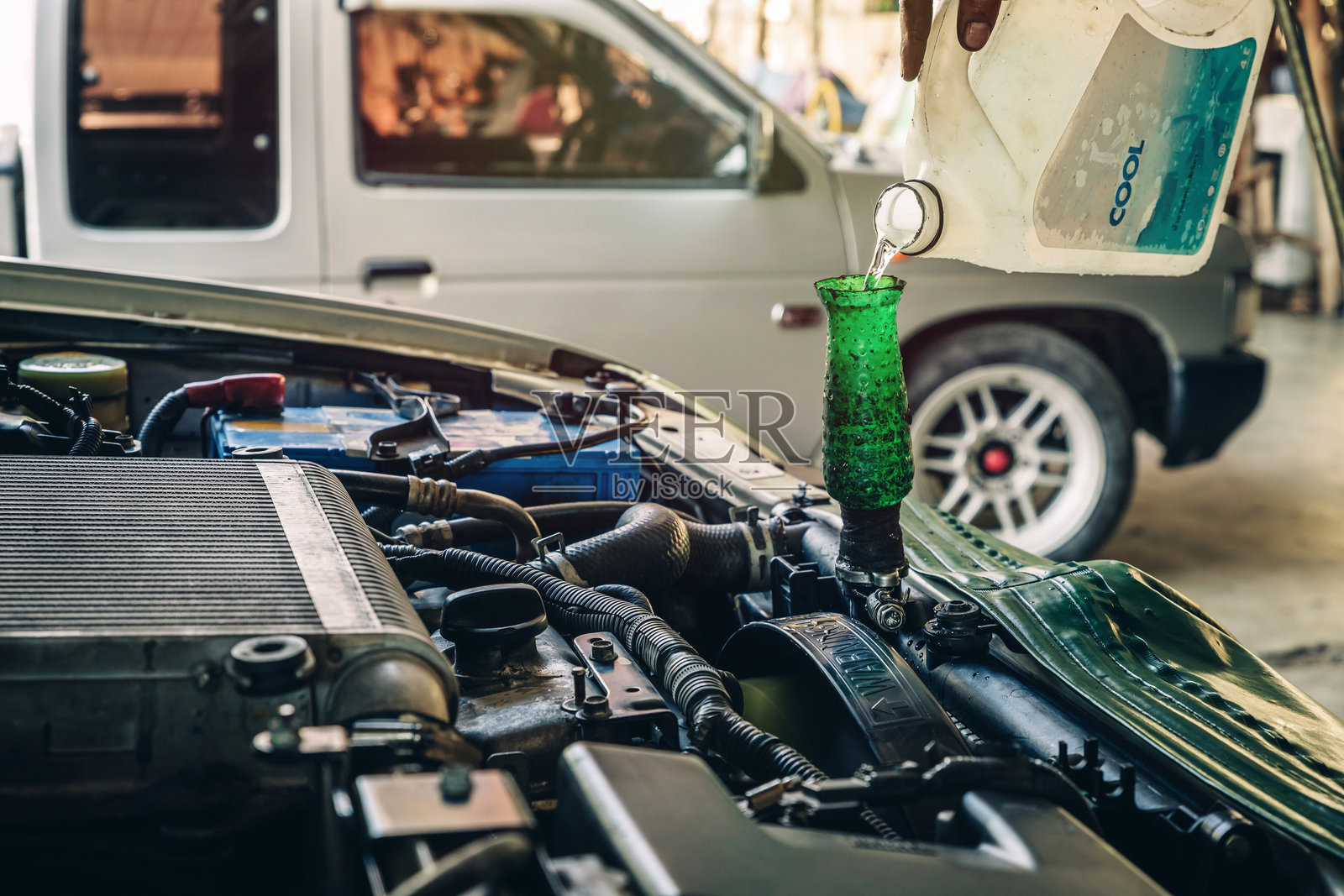 男性专业机械师在服务中心的汽车修理店中将防冻冷却液倒入汽车发动机散热器。汽车散热器冷却液维护的概念。照片摄影图片