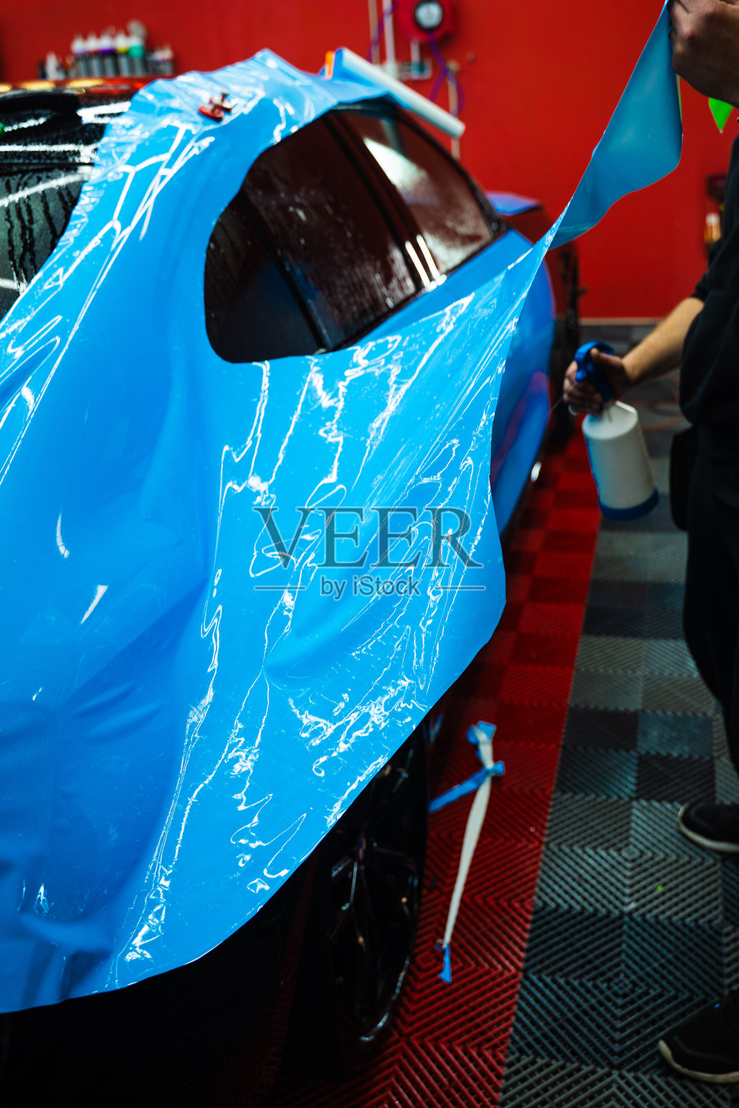 细节处理师使用喷雾辅助方法涂抹鲜艳的蓝色乙烯基包膜，以确保完美无气泡的对齐。细节专家使用水分喷雾来控制蓝色PPF膜的涂抹。照片摄影图片