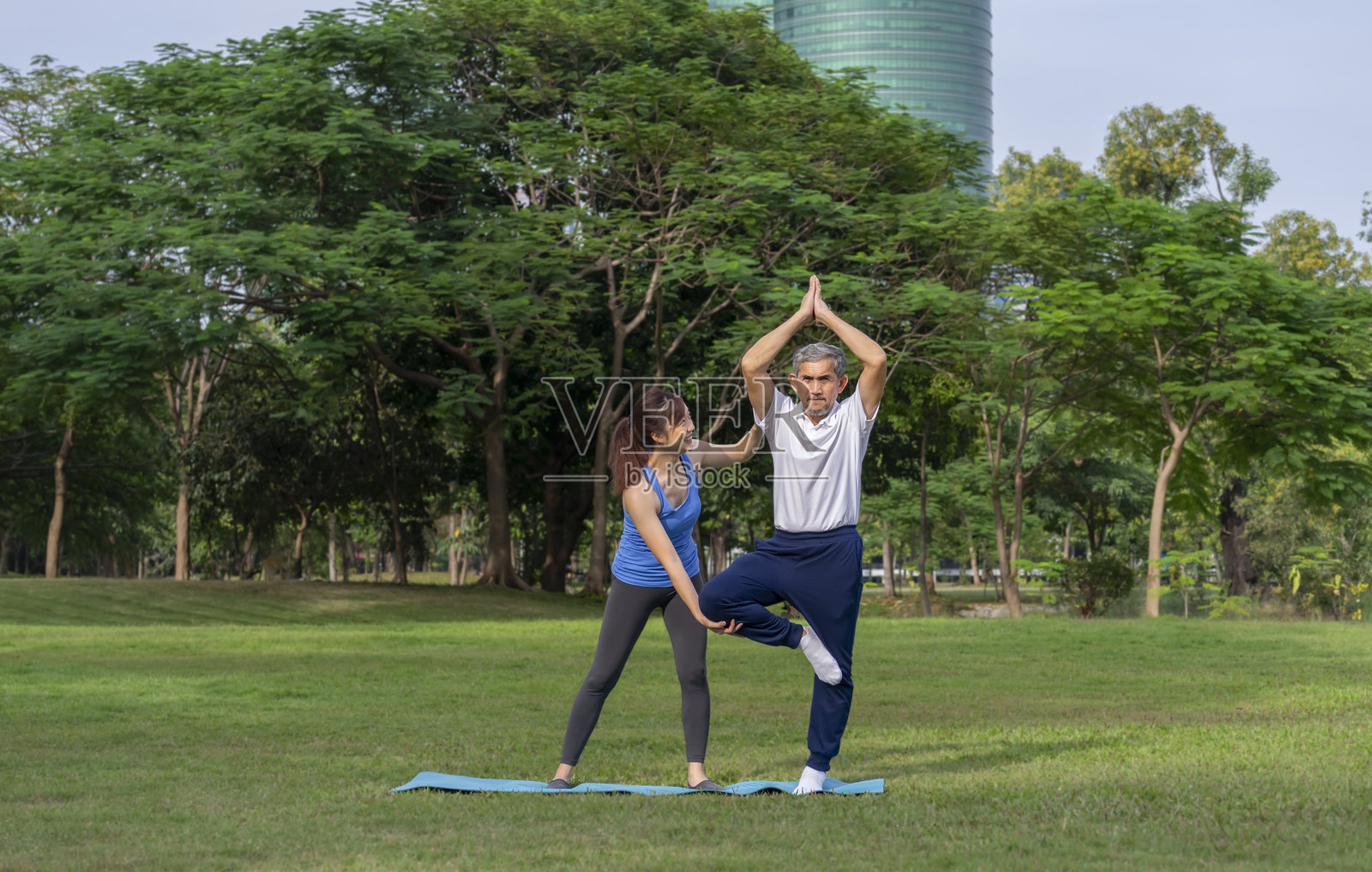 年轻的女儿帮助和支持年长的父亲做瑜伽，快乐的家庭在公园一起锻炼照片摄影图片
