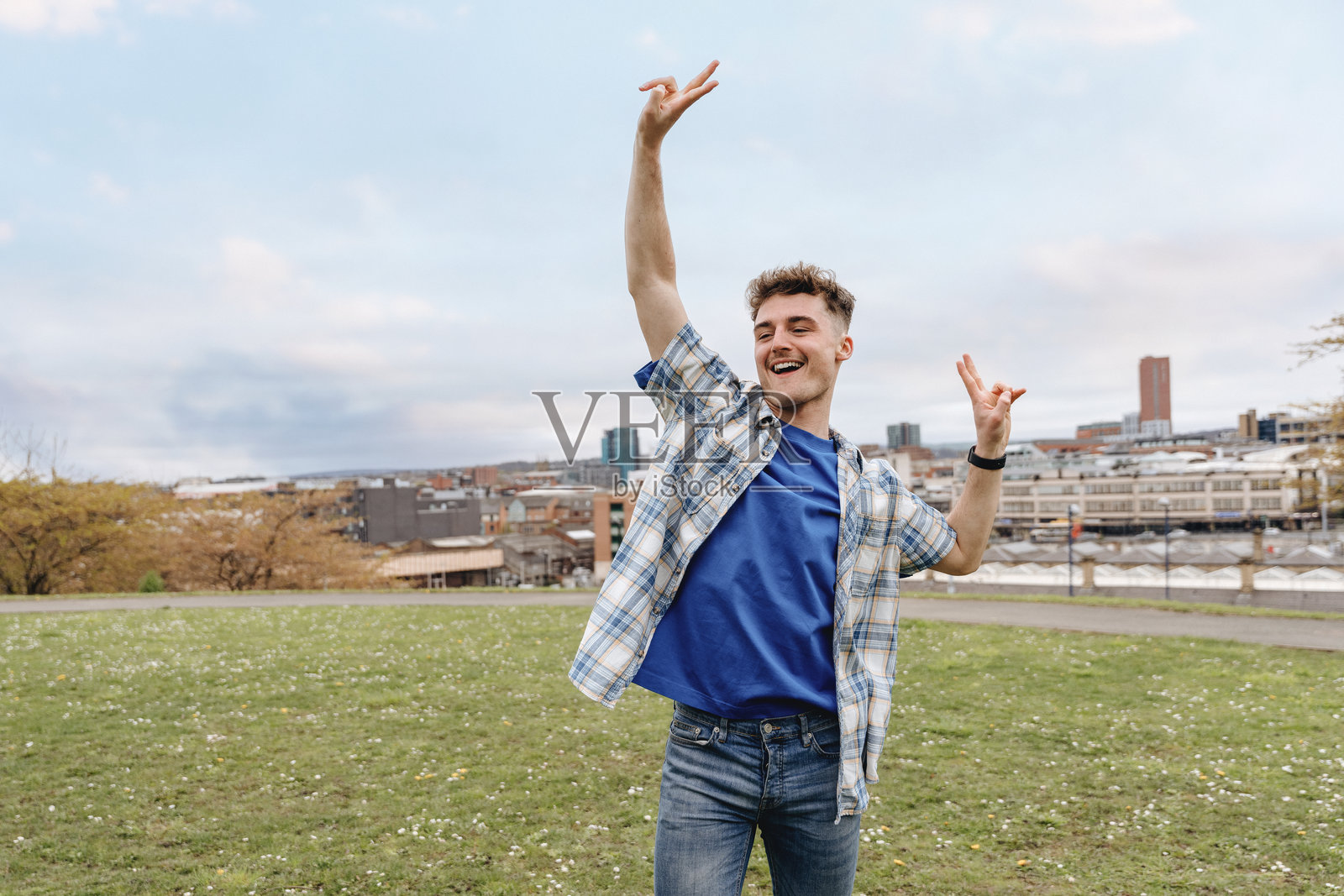 年轻男子在春季阳光明媚的下午，在公园里享受户外舞蹈，背景是蓝天和城市天际线。照片摄影图片