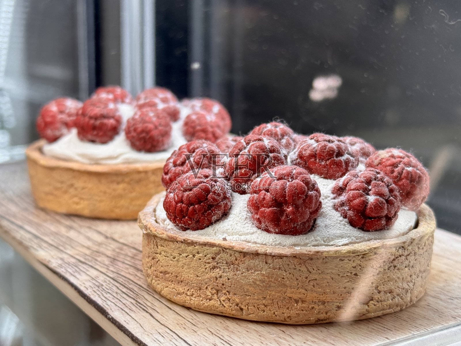 一系列美味的覆盆子挞在温馨的面包店中精美展示。优雅的覆盆子挞上面装饰着丰富的鲜奶油，并轻轻撒上糖粉。照片摄影图片