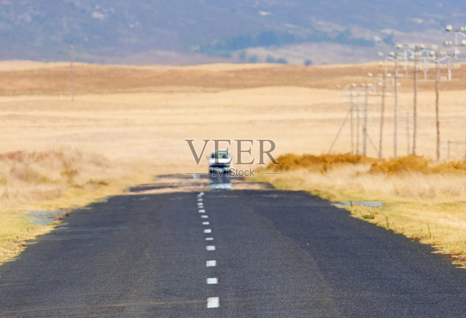 孤独的道路延伸穿过金色田野，通向晴朗日子的地平线。南非。照片摄影图片