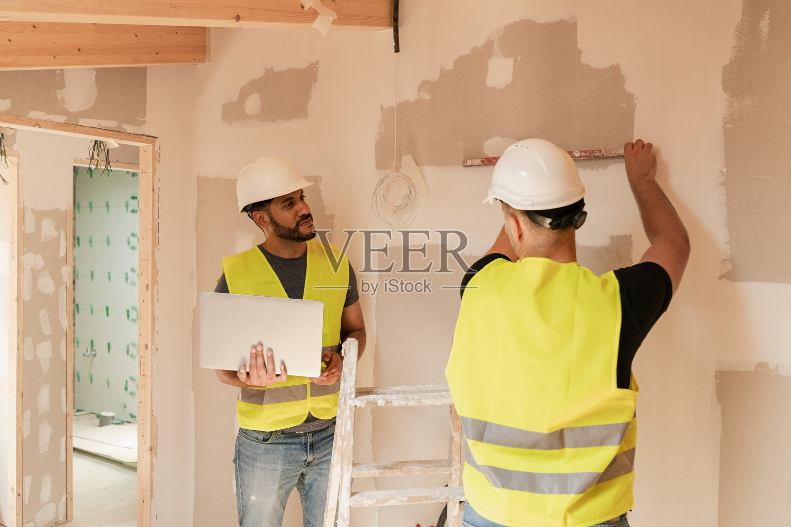 两名男性建筑工人在家居装修期间平整墙壁并使用笔记本电脑照片摄影图片