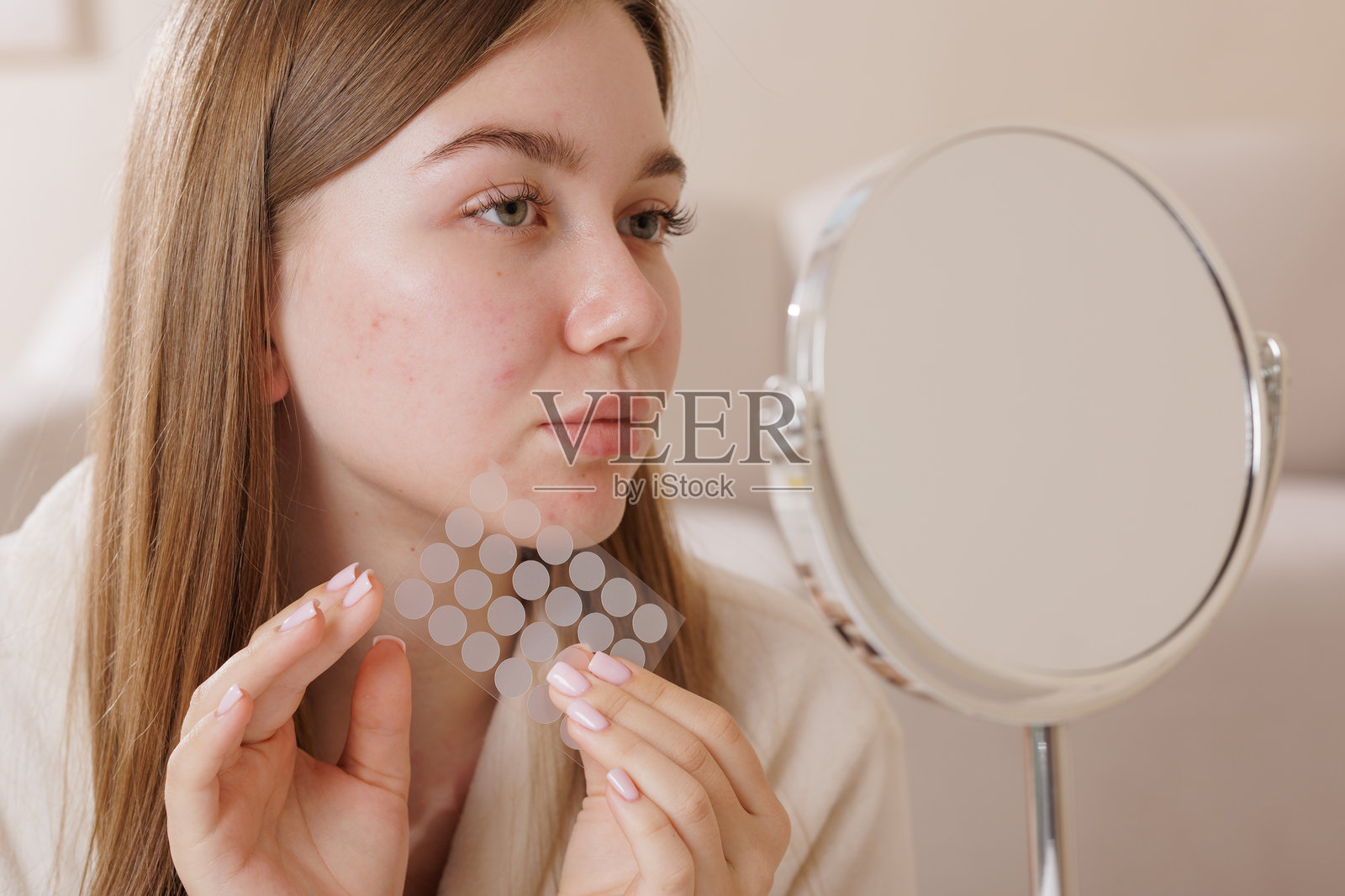 青少年面部有皮肤瑕疵，手持痘痘贴在镜子前，展示现代护肤和自我护理的治疗方法。照片摄影图片