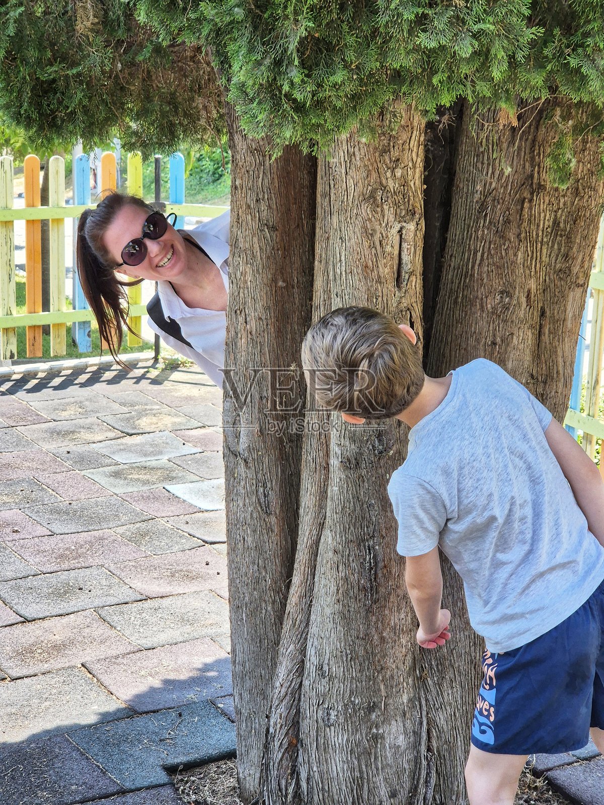 户外游戏。快乐的母亲和儿子在树旁玩捉迷藏照片摄影图片