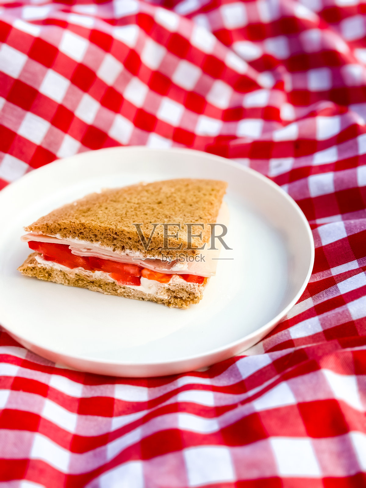 白盘上的火腿奶酪三明治与红色格子野餐布相映成趣照片摄影图片