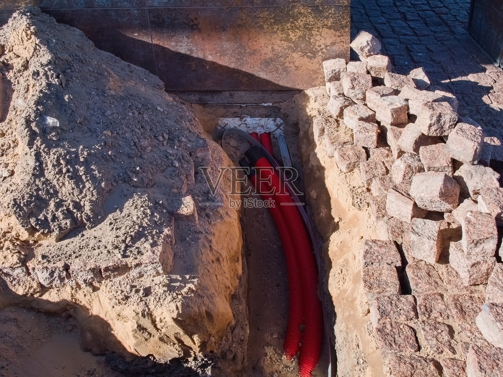 城市地区的地下电缆安装。地基施工中的红色管道。照片摄影图片