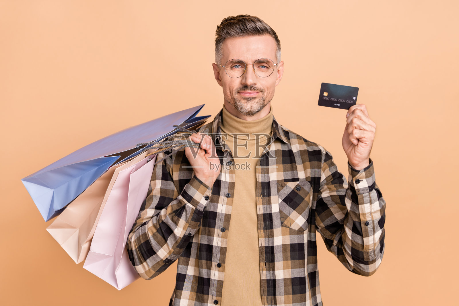 成熟男性高兴地手持包裹，进行借记卡交易，薪水在商场，背景为米色。照片摄影图片