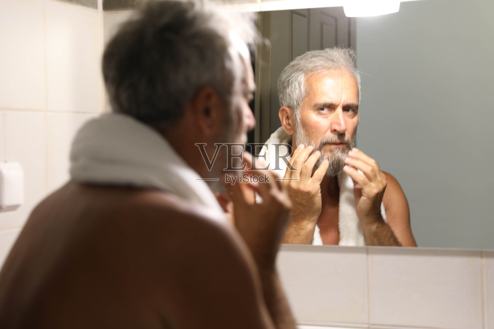 老年男子在家浴室的镜子前看着自己照片摄影图片