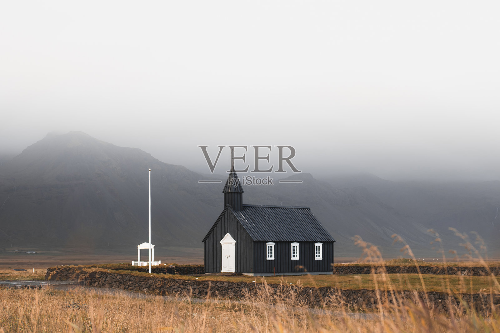 标志性的黑色布达基尔教堂静静地矗立在冰岛西部斯奈菲尔斯半岛的雾蒙蒙的山脉下，成为简单与宁静的永恒象征。照片摄影图片