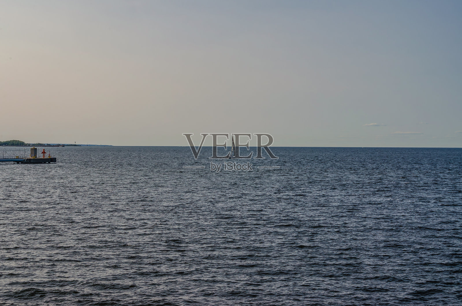 孤独的帆船漂浮在平静的海面上，柔和的日落天空地平线下照片摄影图片