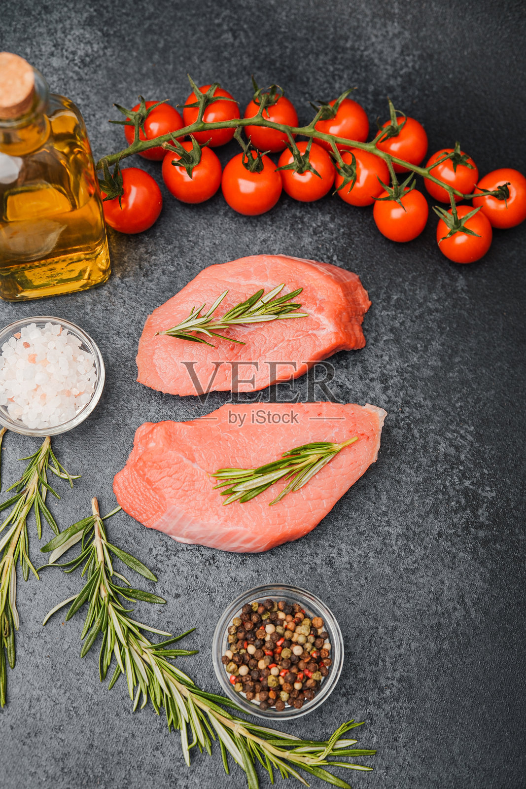 生牛肉排配迷迭香、盐、胡椒和番茄，摆放在深色石桌上照片摄影图片