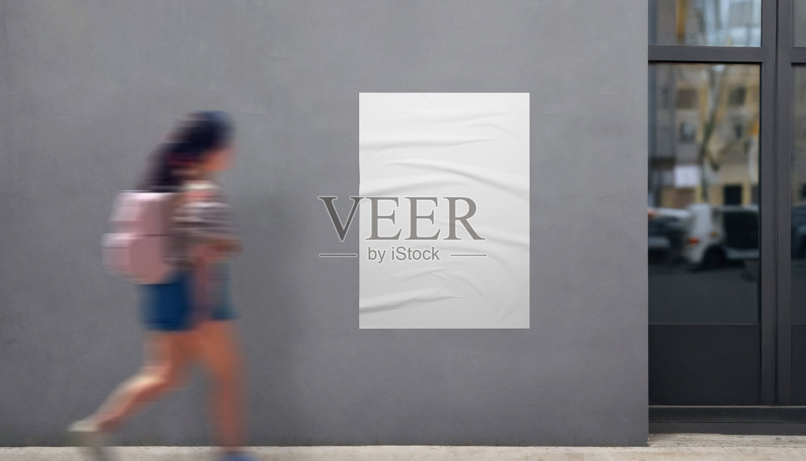 建筑入口旁的白色海报模型。一个背着包的女孩走过，非常适合展示现代宣传海报设计。照片摄影图片