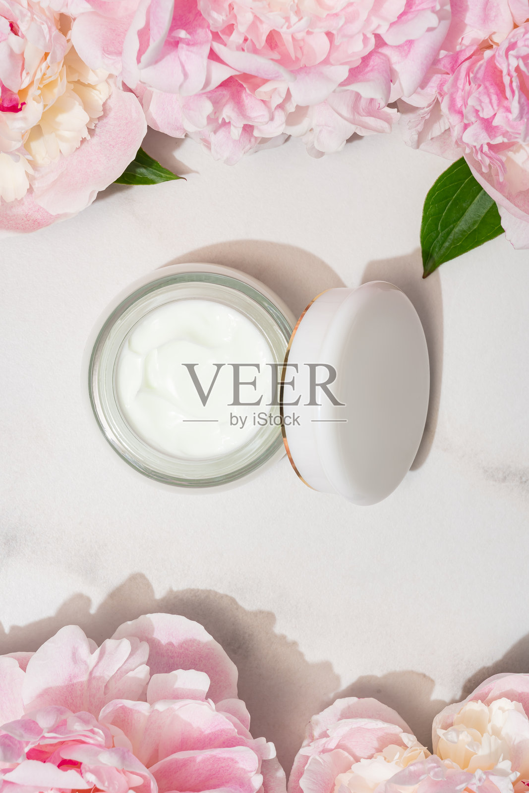 从上方看装有面霜的瓶子和粉色牡丹花。天然有机化妆品概念照片摄影图片