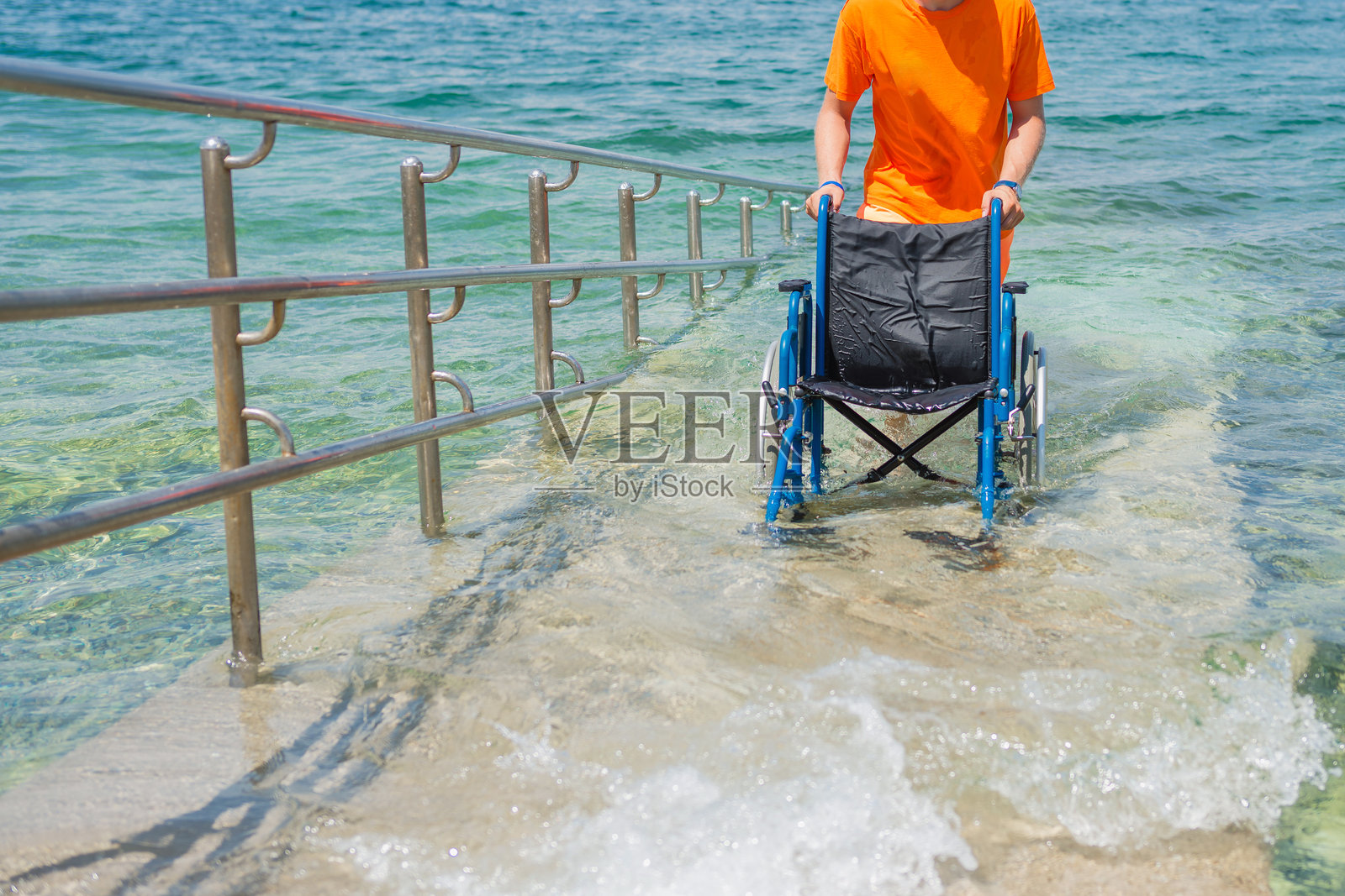 救生员推着一把空轮椅沿着无障碍海滩坡道走出海边照片摄影图片