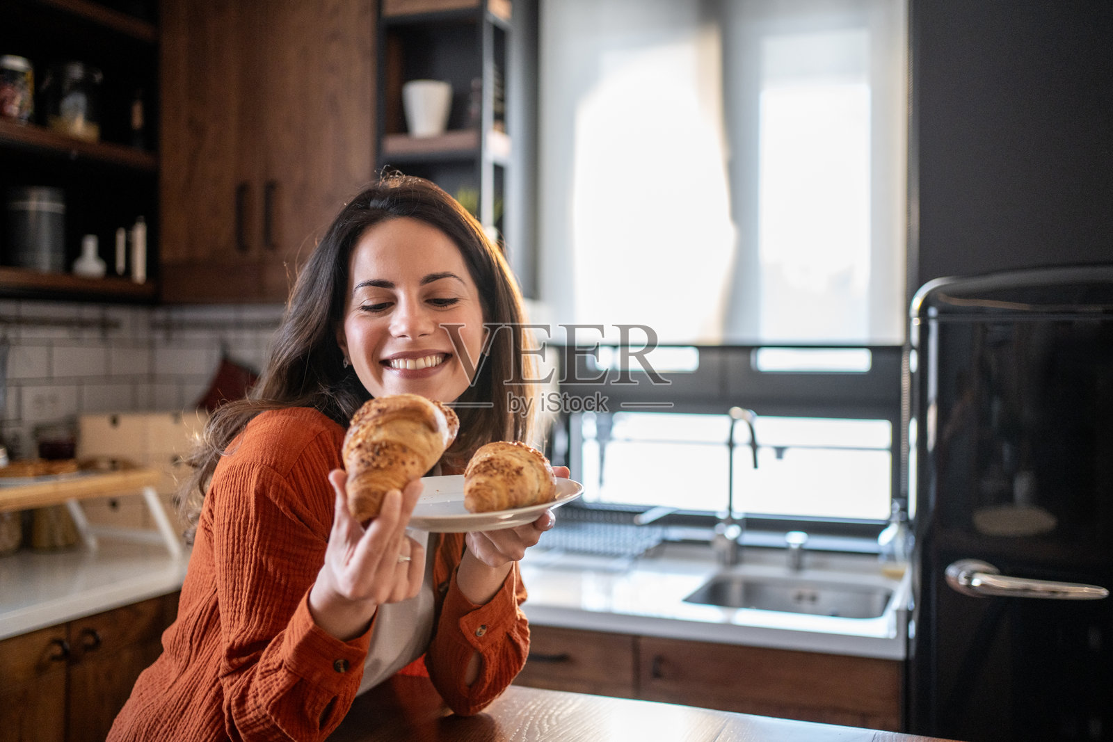 快乐的女人在现代厨房中选择可颂面包作为早餐照片摄影图片