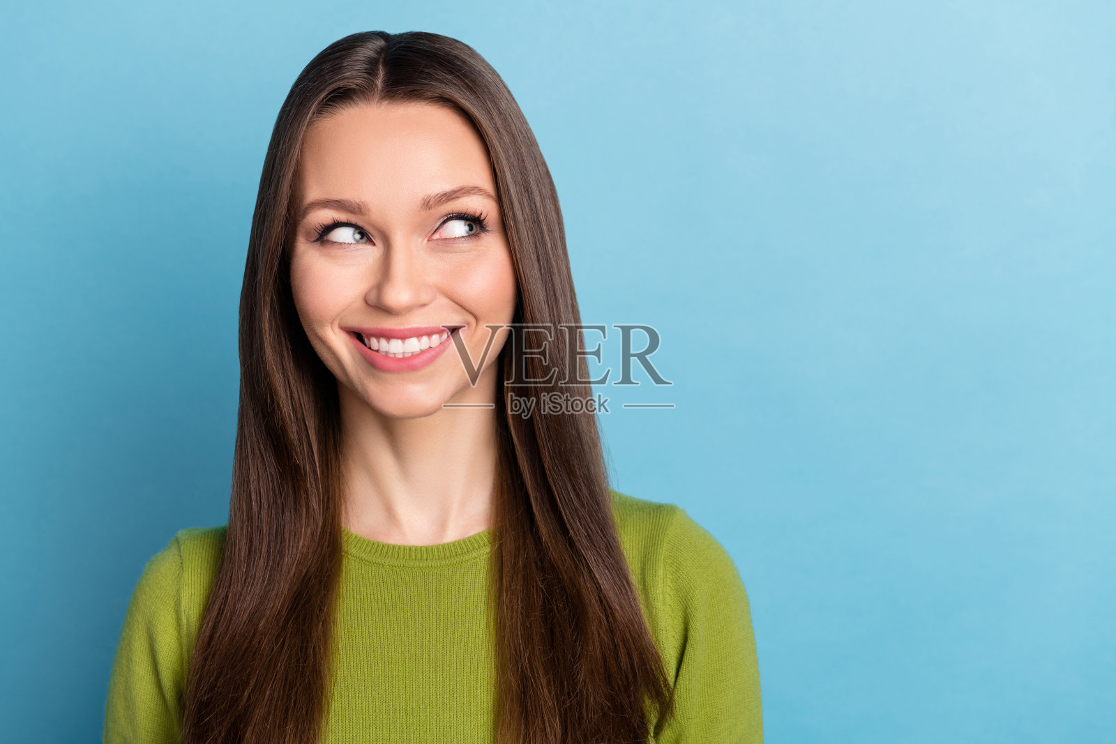 年轻可爱的女孩在蓝色背景下，带着梦幻般的思考神情，凝视着空旷的空间。照片摄影图片