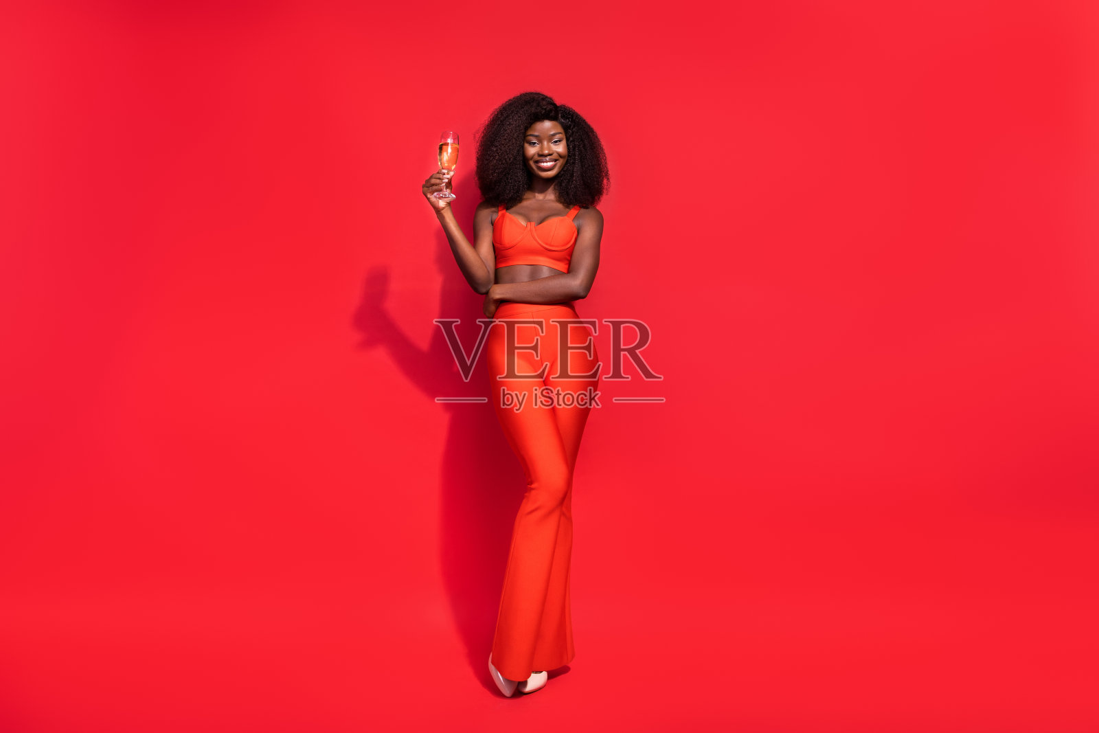 迷人快乐的年轻女士手持香槟酒，享受庆祝时刻，背景为红色。照片摄影图片