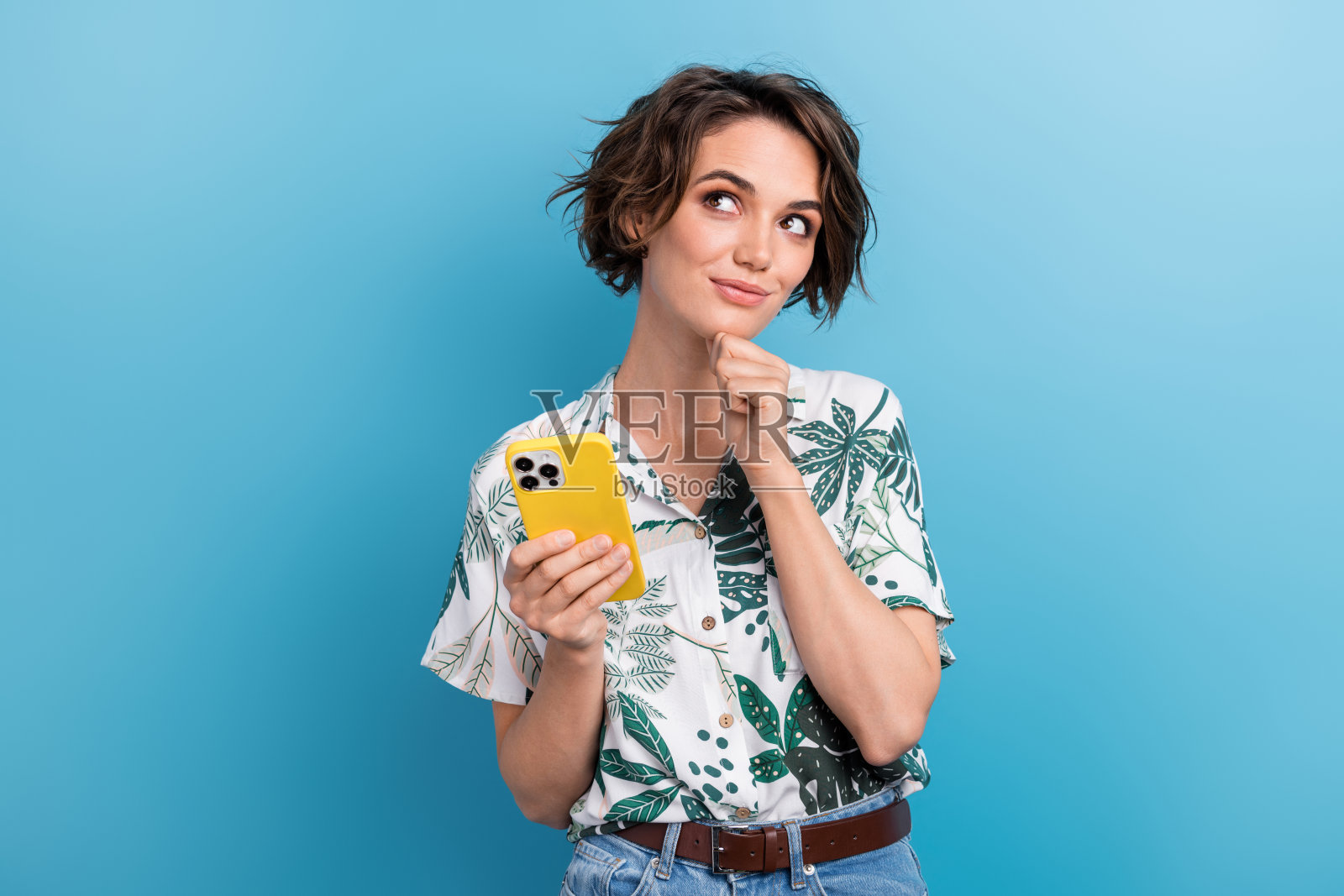 时尚印花叶子服装的可爱年轻女性肖像，站在蓝色背景前，神情专注，目光空灵。照片摄影图片