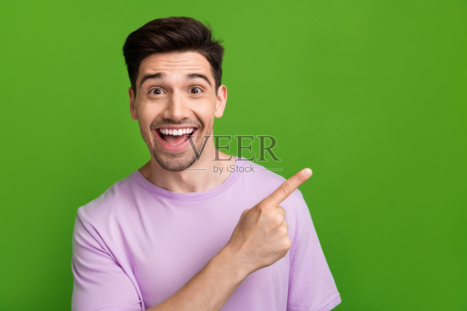 惊讶而快乐的男人穿着紫色时尚服装，推荐产品，空白空间，背景为绿色。照片摄影图片