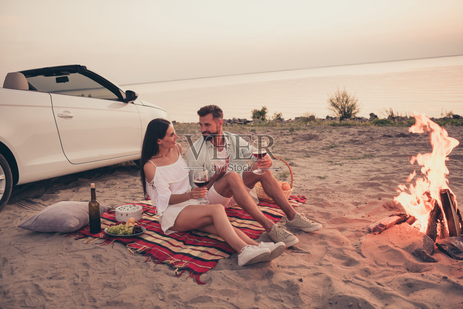 一对穿着白色衣服的美丽甜蜜已婚夫妇在乡间公路上开车，享受红酒，面带微笑。照片摄影图片