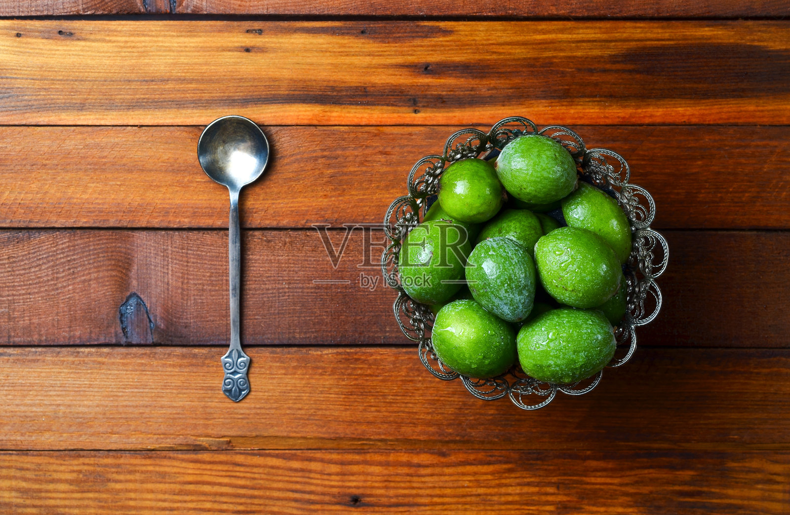 成熟的费约阿果与复古银勺的特写，背景为木质表面。照片摄影图片