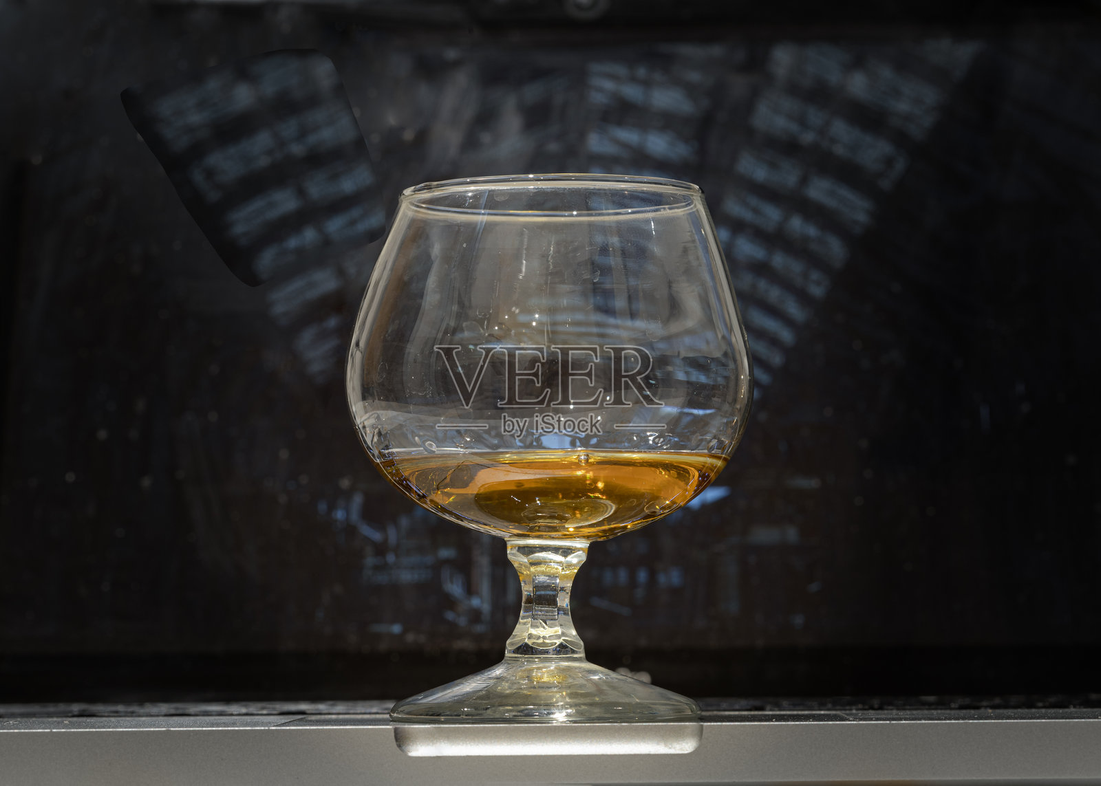 威士忌杯或白兰地酒杯放在笔记本电脑上，背景是笔记本电脑的屏幕。照片摄影图片