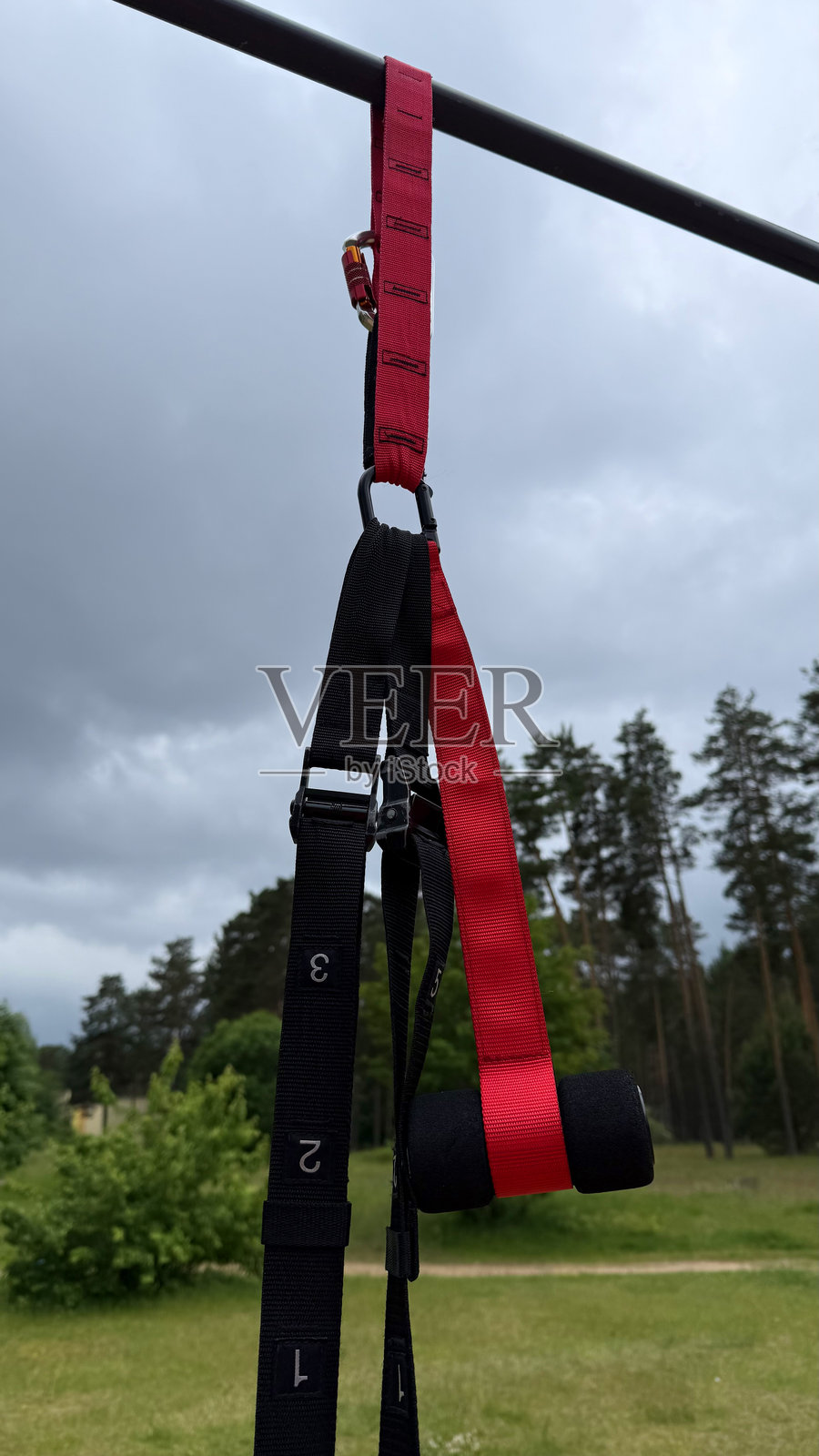户外健身器材上悬挂的TRX悬挂训练带特写，背景是阴 cloudy 的天空 - 体操和健身概念照片摄影图片