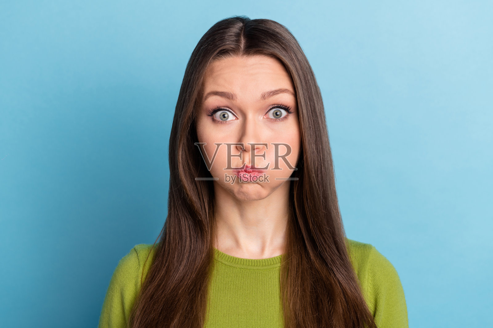 年轻的女孩，圆润的脸颊，憋气做鬼脸，背景为蓝色。照片摄影图片