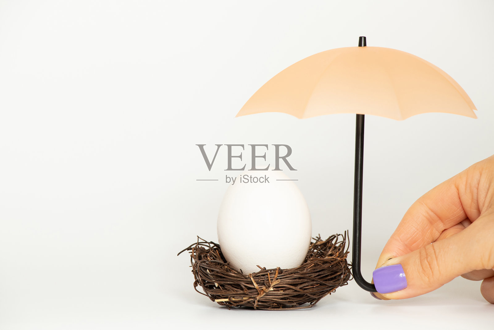 白色背景下，巢中的蛋上方有一把伞，一只女性的手象征着保护和关怀。照片摄影图片