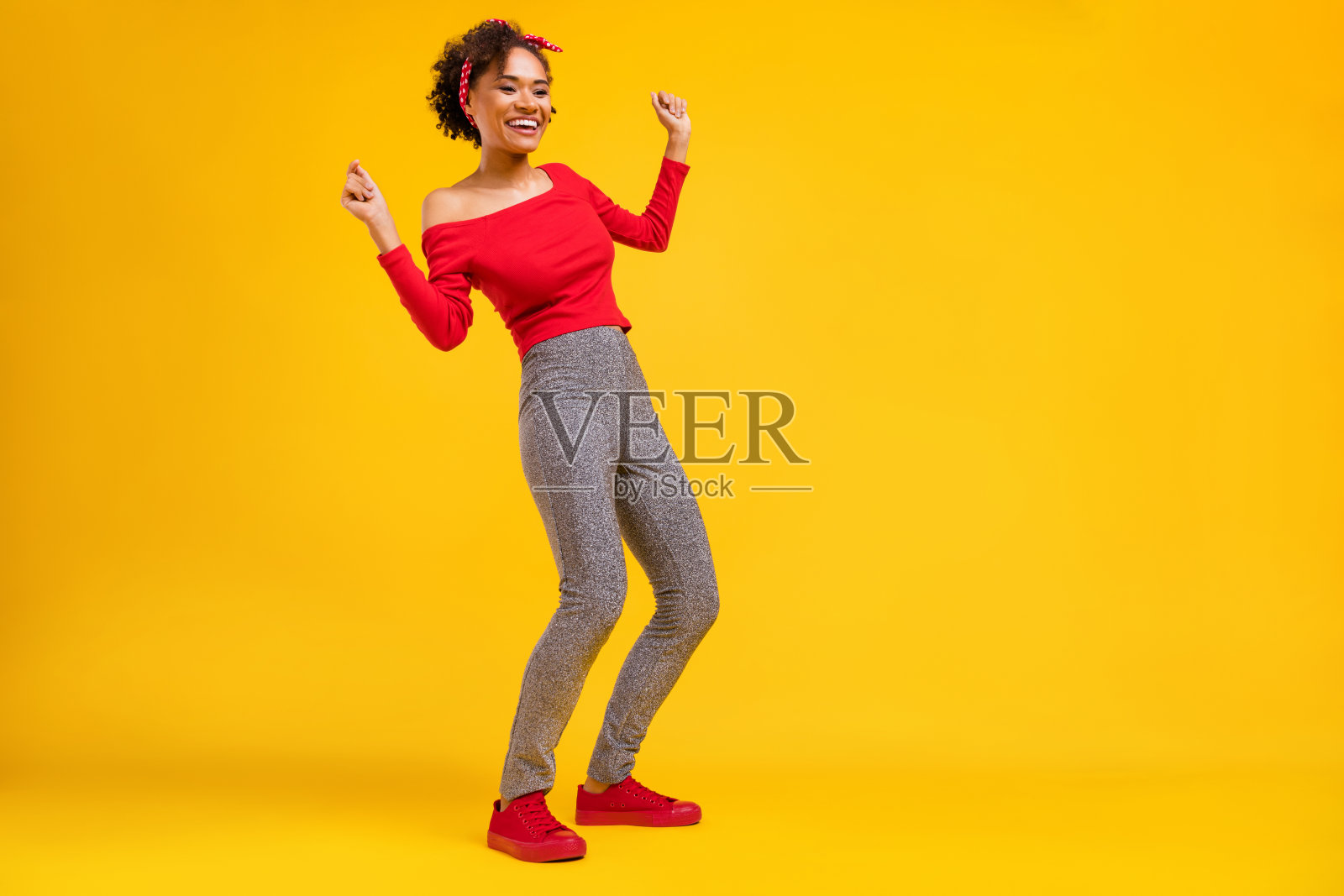 穿着时尚迷人舞蹈服装的积极女性，身着闪亮裤子，背景为黄色。照片摄影图片