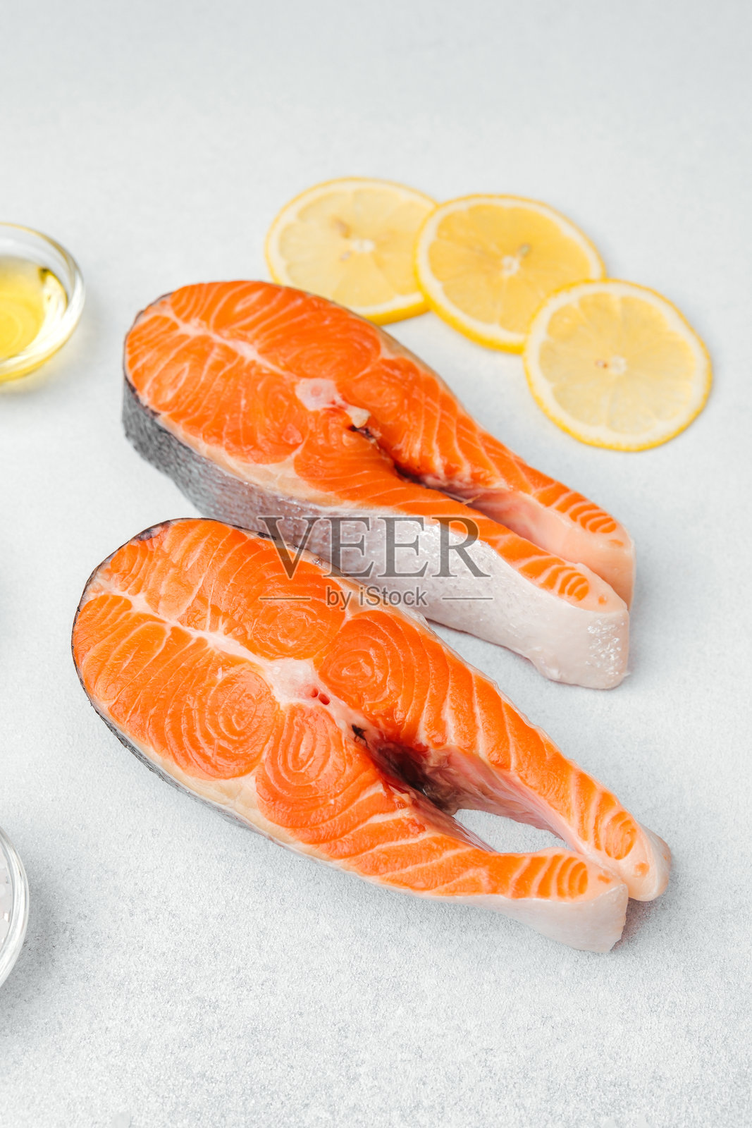 新鲜的三文鱼片准备好烹饪，旁边放有柠檬片照片摄影图片