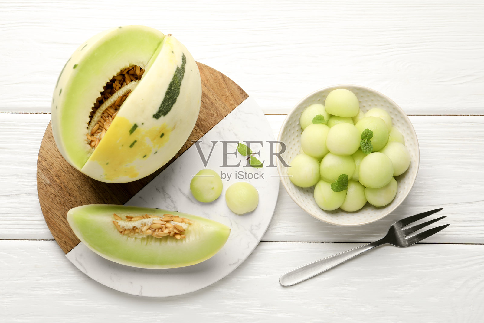 碗里的蜜瓜球和白色木桌上的新鲜水果，俯视图照片摄影图片