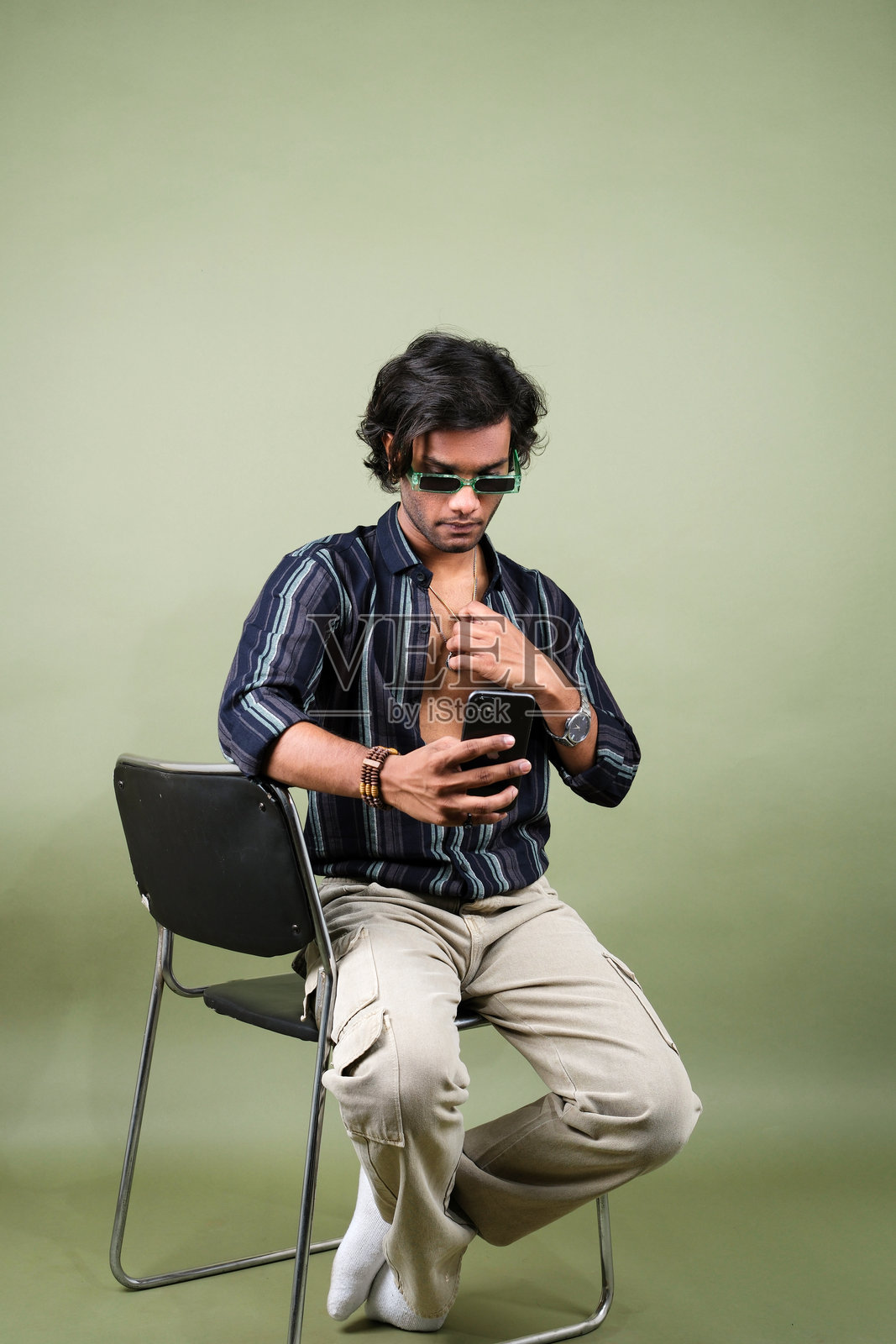 时尚年轻男子穿着条纹衬衫和工装裤，搭配配饰，背景为绿色。照片摄影图片