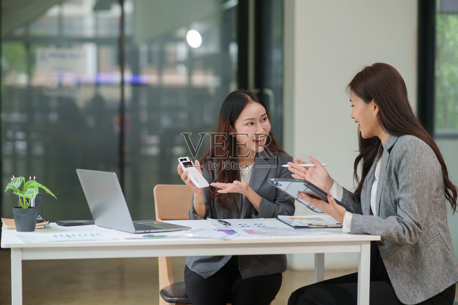 两位亚洲女商人在会议上坐着，讨论投资计划和商业策略。桌上摆放着文件和图表。照片摄影图片