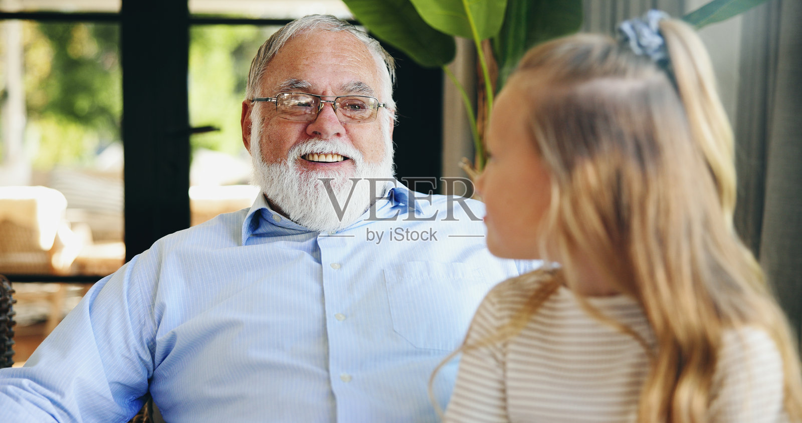 祖孙情深，微笑的爷爷与孙女在客厅交谈。快乐的老人和女孩在家中一起聊天。照片摄影图片