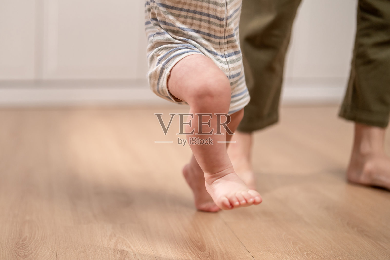 婴儿的小脚丫在地板上迈出第一步，学习走路。可爱的快乐幼儿男孩享受在家温暖地板上学习走路的珍贵时刻，迈出他独立的第一步。照片摄影图片