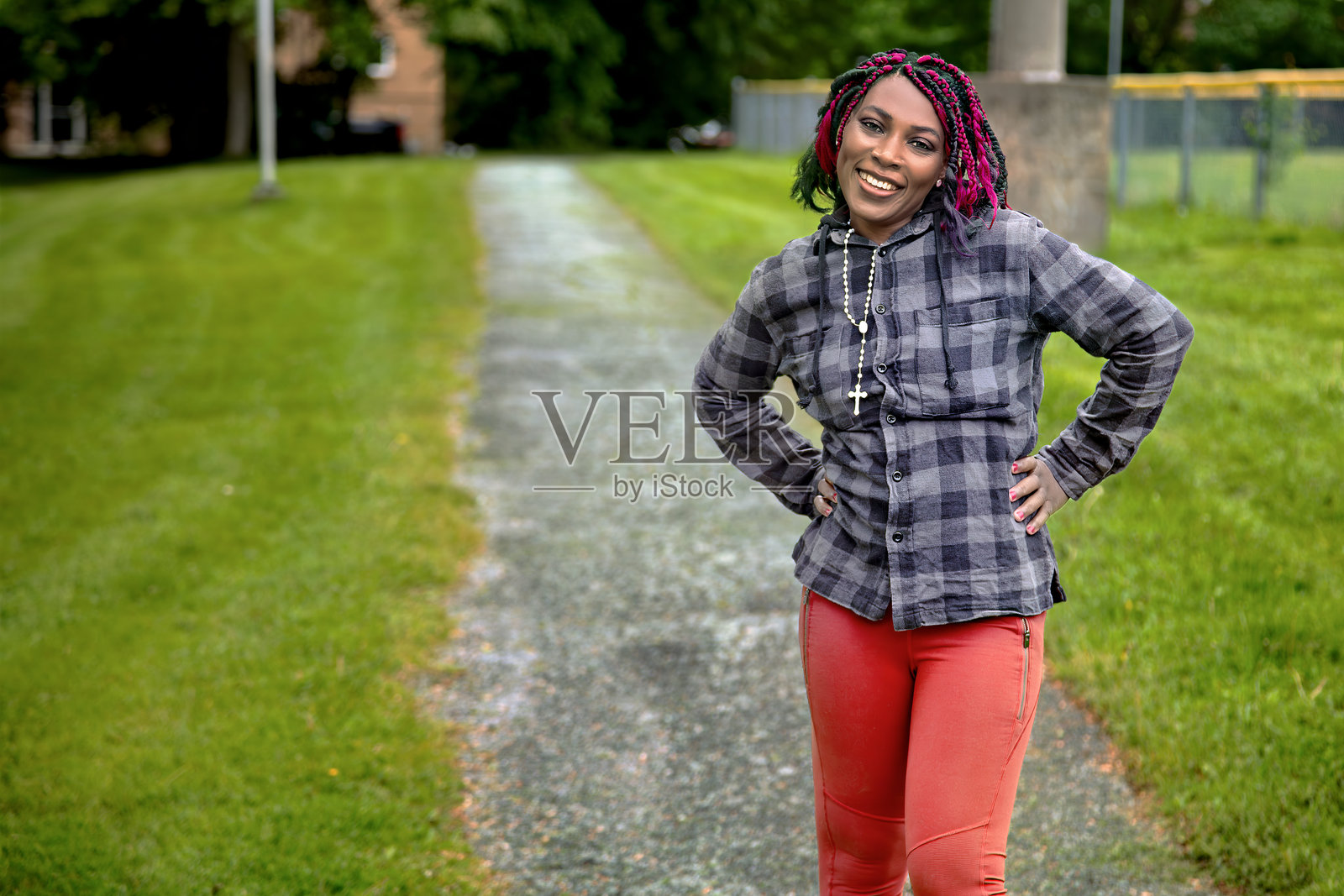 阳光下站在城市公园人行道上的非裔美国女性，扎着辫子照片摄影图片