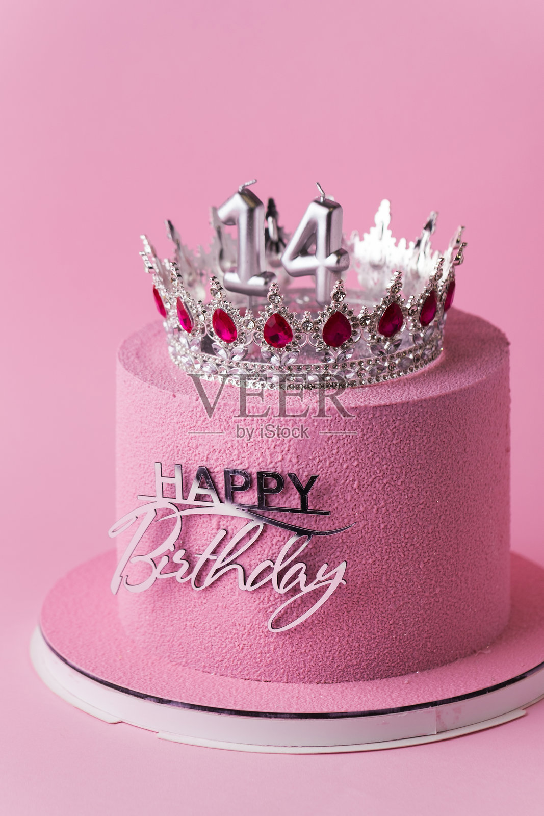 美丽奢华的女孩生日周年蛋糕，外层覆盖粉色巧克力天鹅绒，装饰有银色皇冠和“生日快乐”蛋糕 topper。粉色背景。庆祝14岁快乐的概念。照片摄影图片