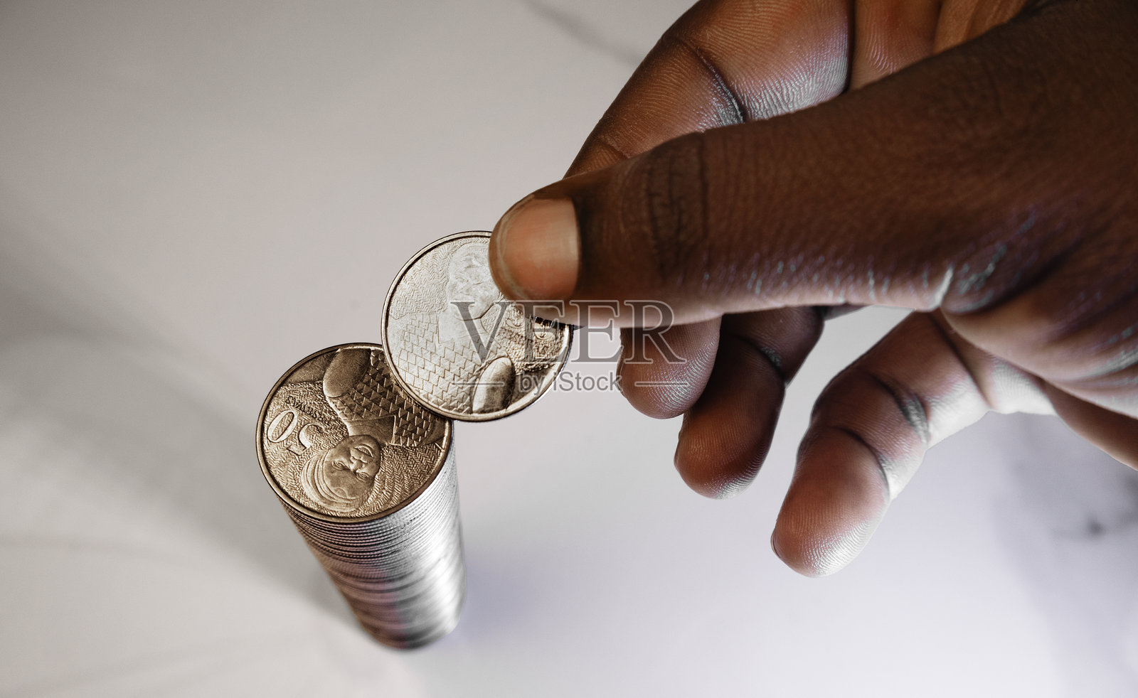 黑人非洲人正在白色大理石桌上将加纳50个佩塞瓦的硬币叠成一长列。照片摄影图片