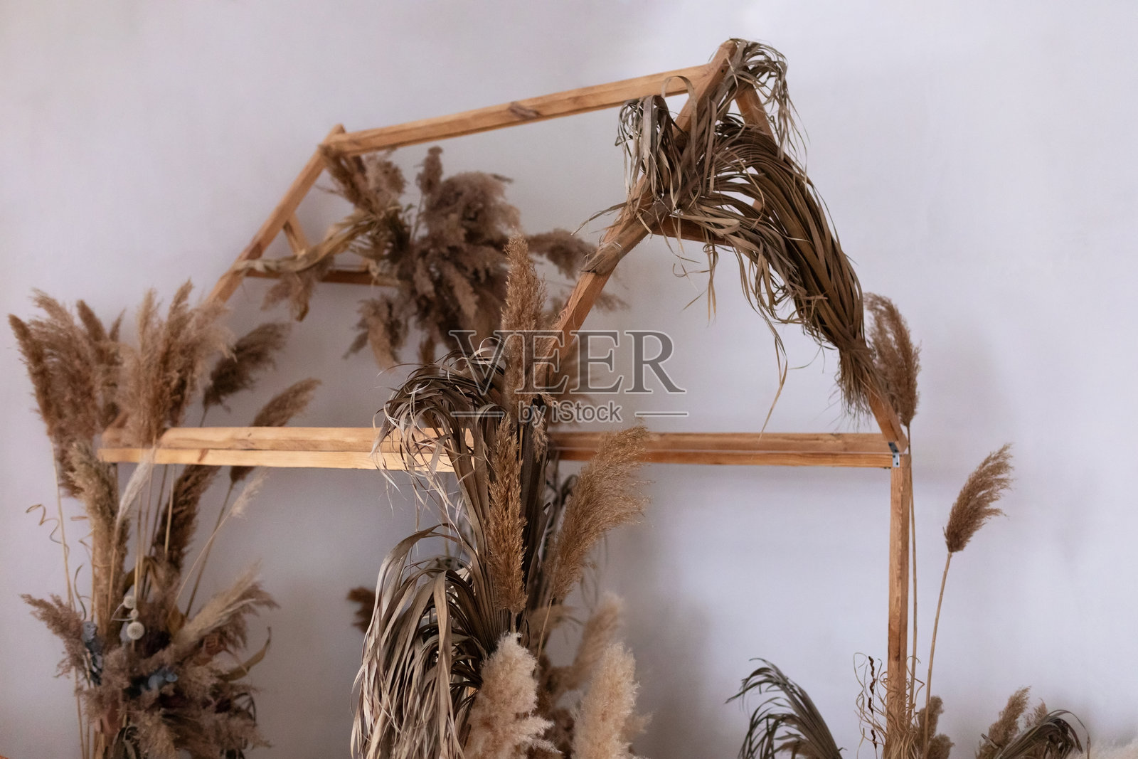 室内木制拱门呈房屋形状，覆盖着干燥的植物和花卉。拱门装饰有植物和芦苇。棕色调的矩形拱门用于婚礼装饰。照片摄影图片