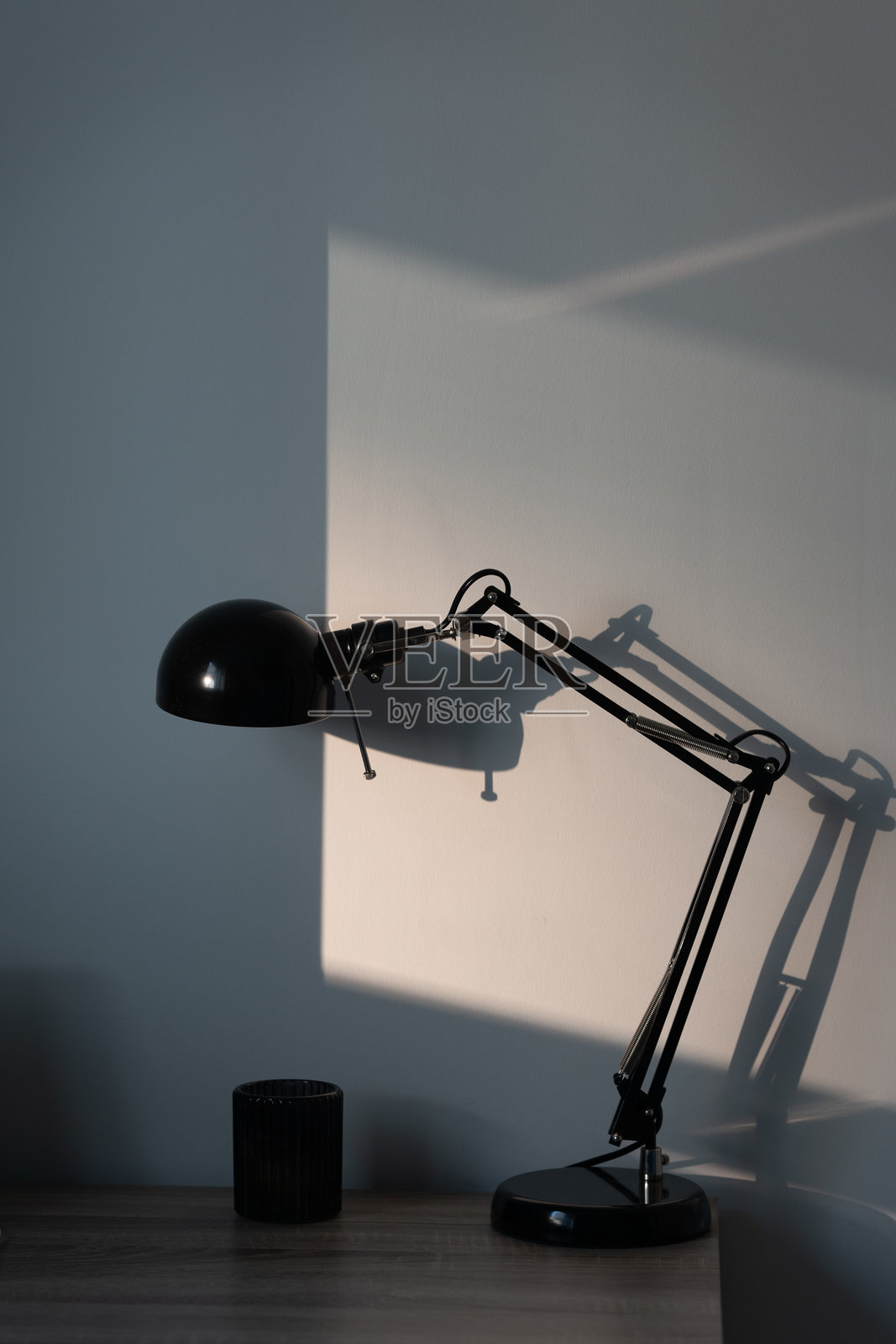 时尚的黑色宜家台灯放在木桌上，背景中阳光的反射。照片摄影图片