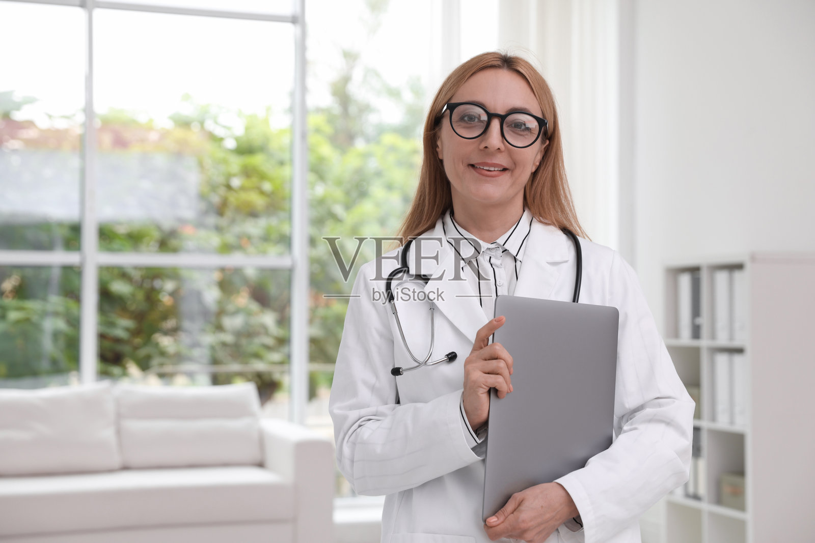 微笑的医生在诊所里拿着听诊器和笔记本电脑照片摄影图片