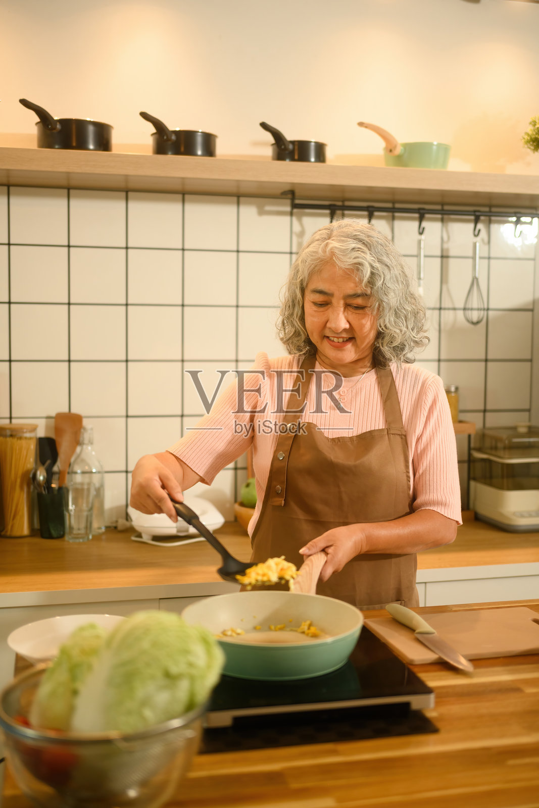 微笑的老年女性在温馨的现代厨房里做炒鸡蛋照片摄影图片