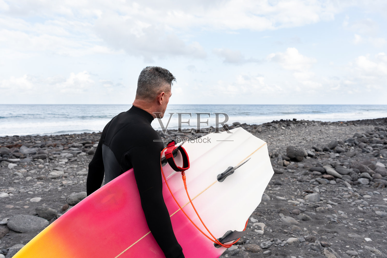 冲浪者在岩石海滩上走着，手持冲浪板观察海浪照片摄影图片