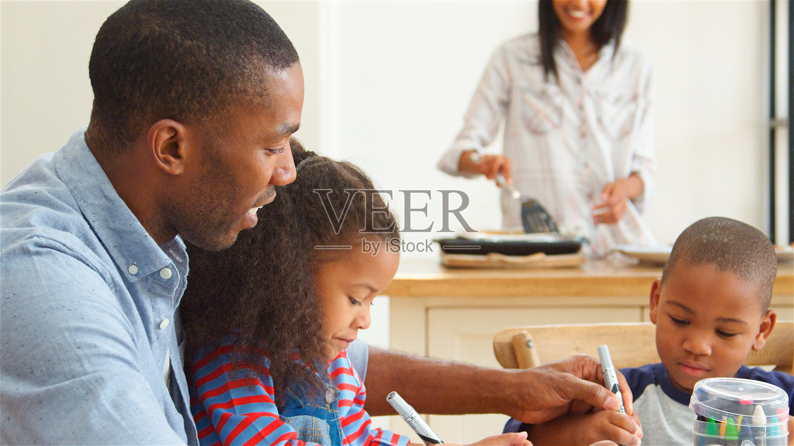 父亲和孩子们在桌子上画画，母亲在准备饭菜照片摄影图片