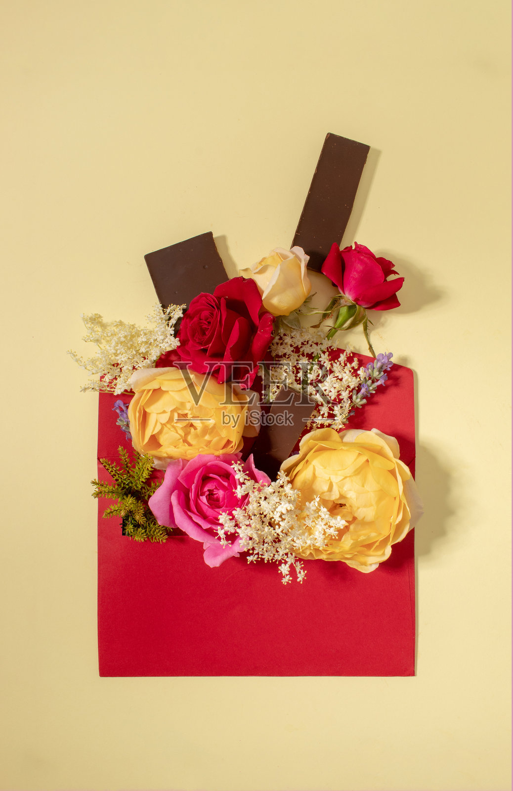 由五彩缤纷的花朵和黑巧克力组成的创意构图，配有红色信封，背景为米色。俯视图，留白空间。照片摄影图片
