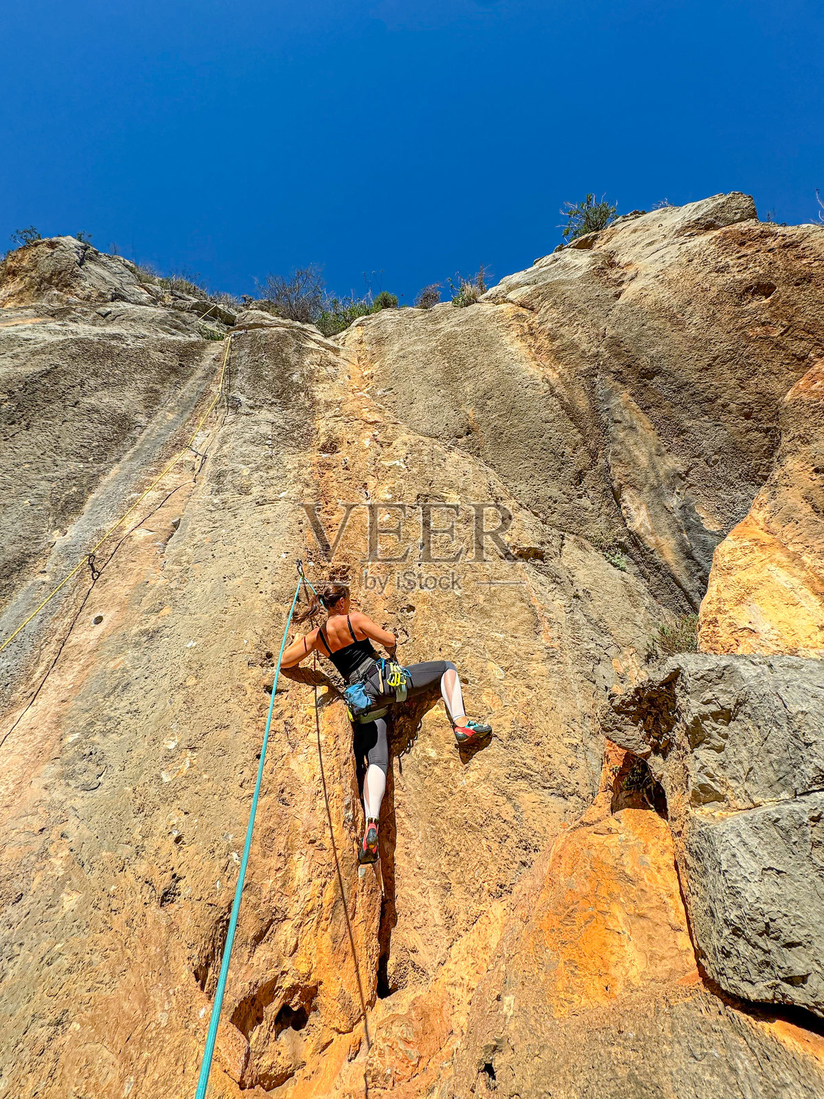 坚定的女性运动攀岩者正在攀爬石灰岩墙。照片摄影图片